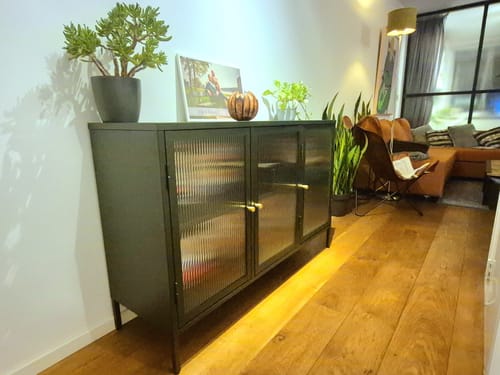 Recensent toont het olijfgroene by fonQ Opal dressoir in een hal, gestyled met planten.
