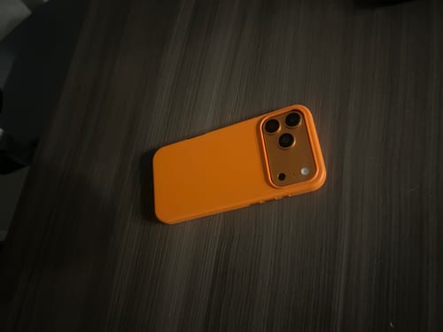 Customer's Ember Orange Signature Leather Magsafe Case for iPhone resting on a dark wood-grain table.