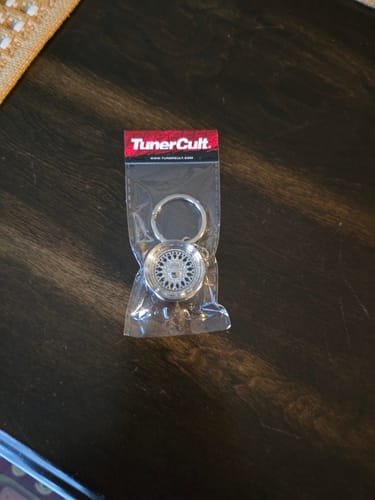 Reviewer's Wheel Keychain shown in its original packaging on a wooden table.