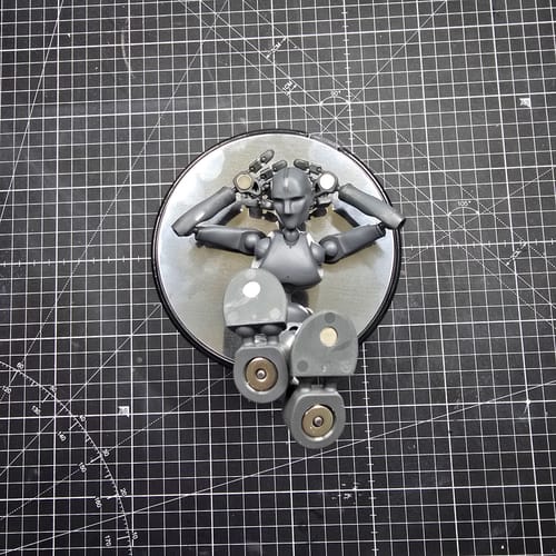 Customer's grey Stickybones figure in a relaxed pose on its round metal baseplate, set on a gridded mat.