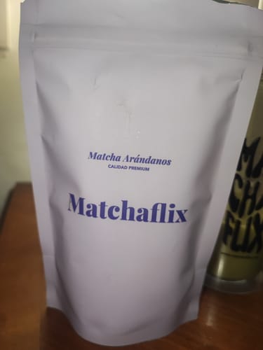 Un cliente muestra la bolsa blanca del Té Matcha Premium Arándanos sobre una mesa de madera.
