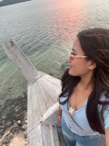 Reviewer wearing the golden oval sunglasses while standing by the water at sunset.