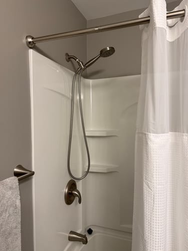 Customer's handheld shower head set installed in a white shower, showing its brushed metal finish.