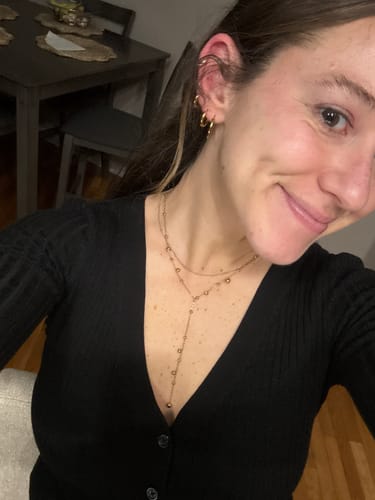 A reviewer smiling while wearing the Lovi Gold Beads Tassel Necklace with a casual black v-neck top.
