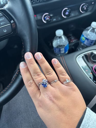 A customer's hand wearing the Navae Birthstone Ring with its blue pear and clear radiant-cut stones.