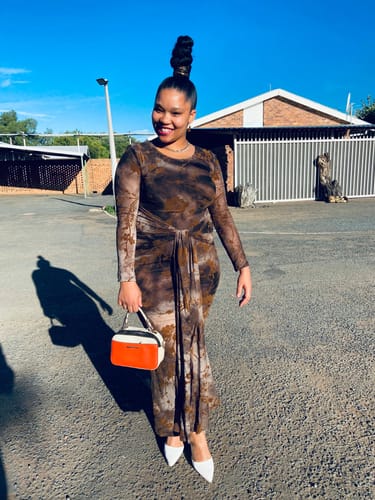 Reviewer smiling outdoors in the patterned Draped Knotted Waist Mesh Maxi Dress, paired with white heels.