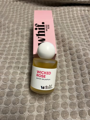 Customer's Wicked Rose perfume bottle with its white cap, next to the pink product box on a textured surface.