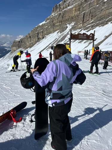 Reviewer from behind wearing baggy black Snow Pants, holding a snowboard on a snowy mountain.