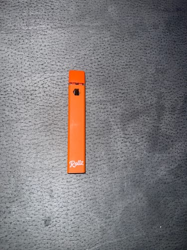 Customer's orange ROLLZ THCA Vape pen lying on a textured gray surface.