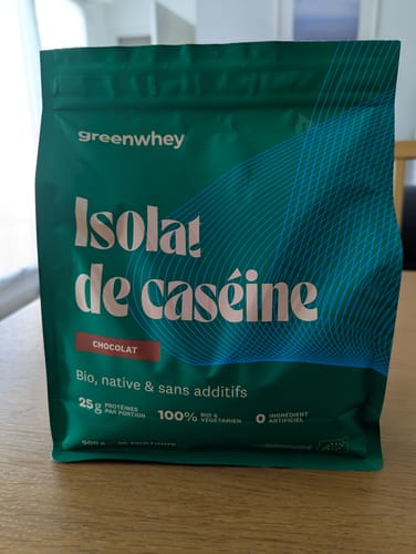 Un client montre son sachet vert d'Isolat de Caséine saveur chocolat sur une table.