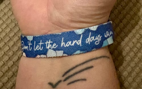 Close-up of a customer's wrist wearing the blue patterned 'Don't Let the Hard Days Win' bracelet.