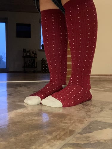En kunde viser sine røde, prikkede støttestrømper på et flisegulv.
