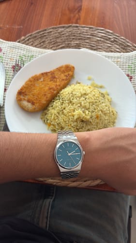 Cliente mostrando su reloj Casio Análogo con esfera azul y correa de acero en la muñeca, frente a un plato de comida.