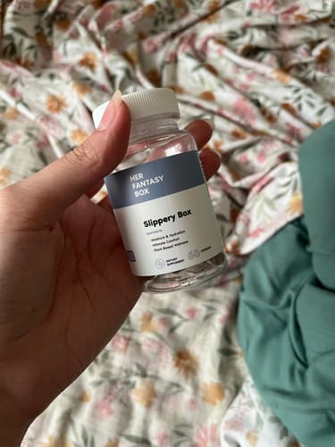 Customer holding a clear bottle of Slippery Box capsules against a floral background.