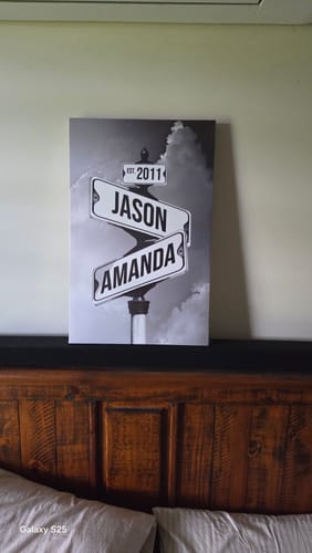 Customer's personalized black and white 'Date of Love' canvas with names and a date, resting on a dark wood headboard.