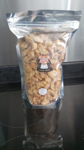 Customer's large, clear bag of Big 'n' Mix pork scratchings standing upright on a dark, reflective surface.