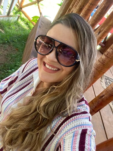 Avaliadora sorrindo em uma selfie usando os Óculos Veneza com armação preta e lentes em degradê.