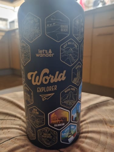Customer's black World Explorer Bottle with gold engravings of world destinations and a few colorful stickers applied over them.