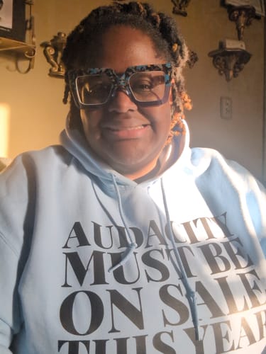 Reviewer smiling in their light blue Audacity Hoodie, with the text 'Audacity Must Be On Sale This Year' visible on the front.