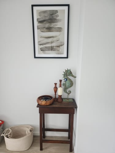 Customer's Pebble I Art Print in a black frame hanging on a white wall above a small wooden side table.