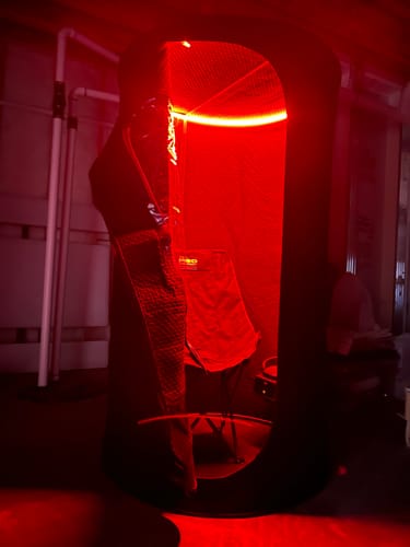 Customer's Sauna Pod set up indoors, glowing with its bright red ambient light feature on.