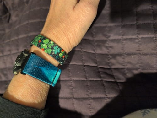 A reviewer's wrist wearing the Lucky You Bracelet with its green clover pattern next to a watch.
