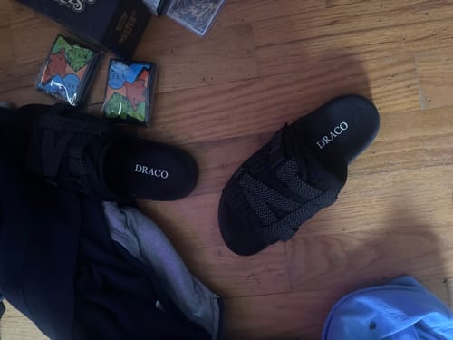 A customer's pair of black Reflective Dracoslides with woven straps, seen on a wooden floor.