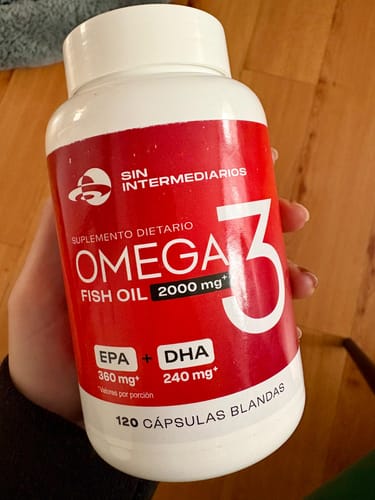 Cliente sosteniendo el frasco de Cápsulas Omega 3, mostrando la etiqueta roja y blanca del producto.