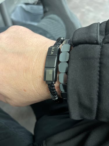 A reviewer wearing the R.E.D. Tiger's Eye Never Forget Bracelet, showing the engraved black metal clasp on their wrist.