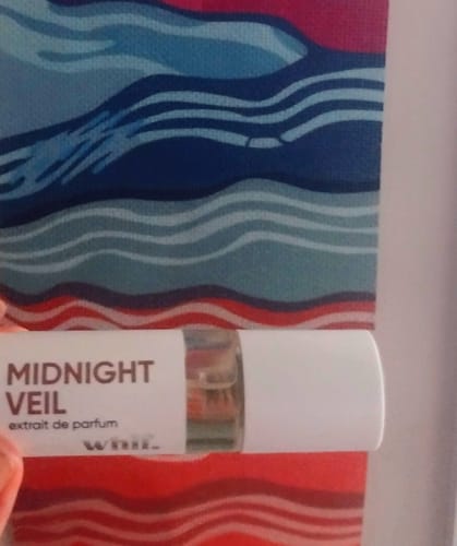 Close-up of a customer holding a small vial of Midnight Veil perfume against a patterned background.