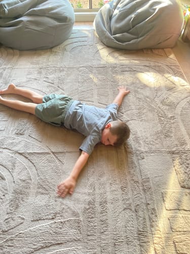 Customer's child making a snow angel on the soft, carved Mellow Mat® in a sunlit room.