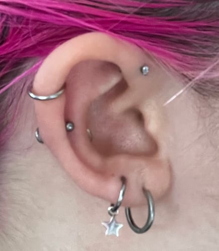 A reviewer's ear with multiple piercings, highlighting the Small Solitaire flatback Silver stud in the forward helix.
