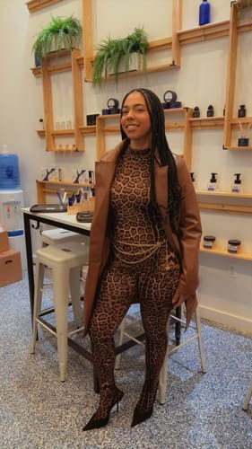 Customer wearing the leopard print Naked Print Closed Toe Jumpsuit, styled with a brown coat and a thin gold chain belt.
