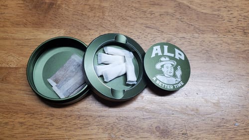 Reviewer's open green travel tin holding Mountain Wintergreen Nicotine Pouches and another pouch type.