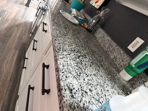 Customer shows off a shiny, clean granite countertop after using a cleaner from the Home Starter Bundle.