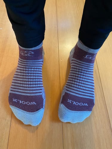Reviewer wearing the striped Amelia No Show Socks in Grape Harvest and grey, paired with black leggings on a wood floor.