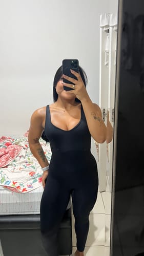 Avaliadora mostrando o caimento do Macacão Decote Costas preto em uma selfie no espelho.