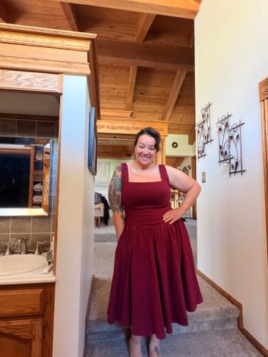 Reviewer smiling while wearing the ruby red Bombshell Swing Dress indoors, showing the square neckline and fit.