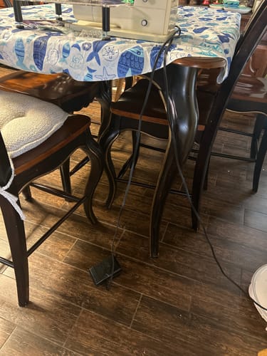 Reviewer's Bernina foot control and cord set up, with the black pedal on the floor below a sewing machine on a table.