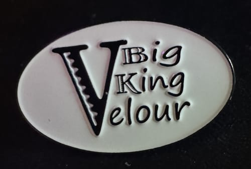 A customer's custom enamel pin with a white oval design and black raised text reading 'VBig King Velour'.
