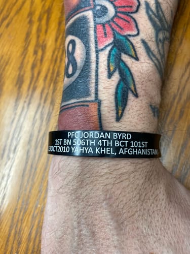 Close-up of a reviewer wearing the custom black bracelet, showing the engraved text memorializing PFC Jordan Byrd.