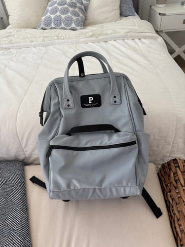 Reviewer's light blue Cascade Backpack with black trim, sitting upright on a bed.