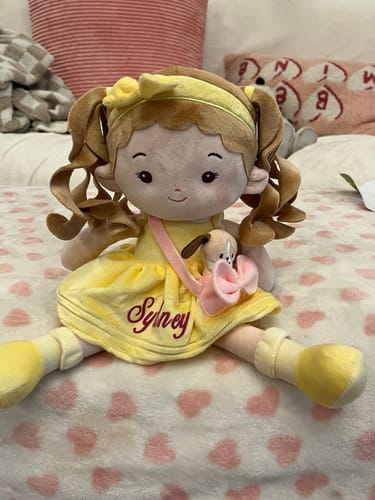 Customer's Personalized Sunny Girl doll in a yellow dress embroidered with the name 'Sydney', sitting on a heart-print blanket.