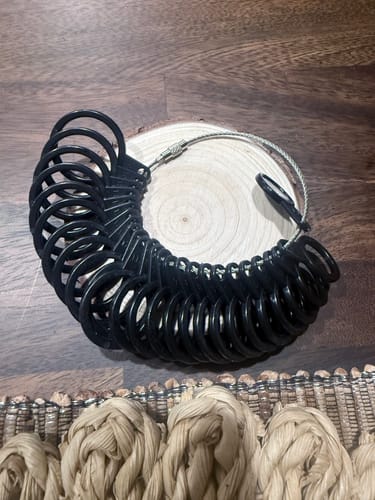 A customer's Thorum Ring Sizer, a set of black rings on a wire loop, resting on a wooden slice.