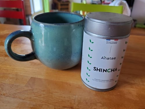 Avis d'un client : la boîte de thé Shincha Bio posée à côté d'une tasse bleu-vert sur une table en bois.