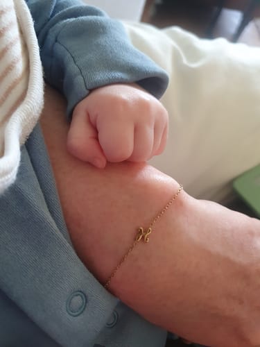 Reviewer's wrist showing the delicate Initial Chain Bracelet, with a baby's small hand resting on their arm.
