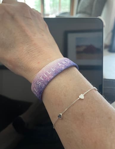 A close-up of a reviewer's wrist wearing the purple and pink 'Be Still And Know' Bible Verse Bracelet.