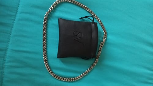 Cliente mostrando la brillante Cadena Cuban Link junto a su funda sobre una tela turquesa.