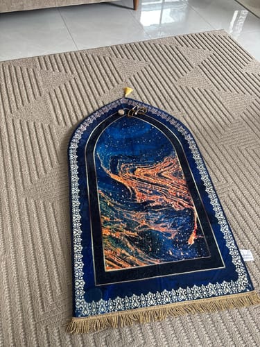 Customer's Qibla-Cosmos padded prayer mat with a blue and orange cosmic design laid on a rug.