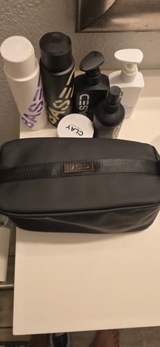 Customer's black Toiletry Bag on a bathroom counter in front of several grooming products.